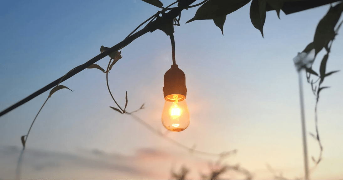 夕暮れの空を背景に、暖かく光る一球の吊り下げ電球_メインビジュアル_pc
